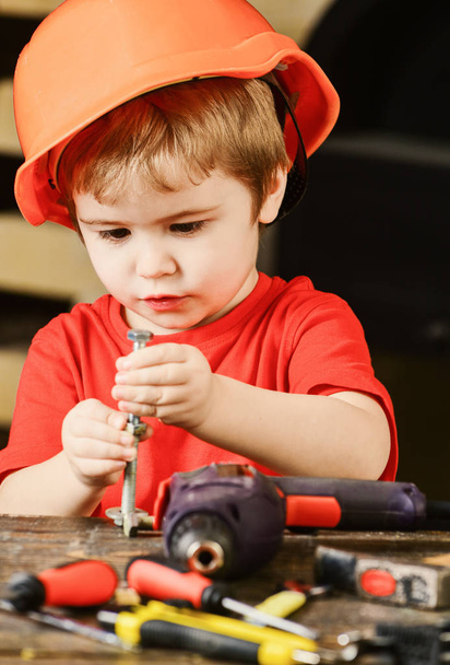 Child in hard hat, helmet playing with hex bolts as builder or repairer, handcrafting. Toddler on busy face plays with bolts at home in workshop. Kid boy play as handyman. Handcrafting concept - Photo, Image