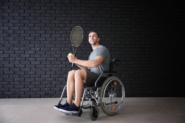 Молодой теннисист сидит в инвалидной коляске на стене из темного кирпича
 - Фото, изображение