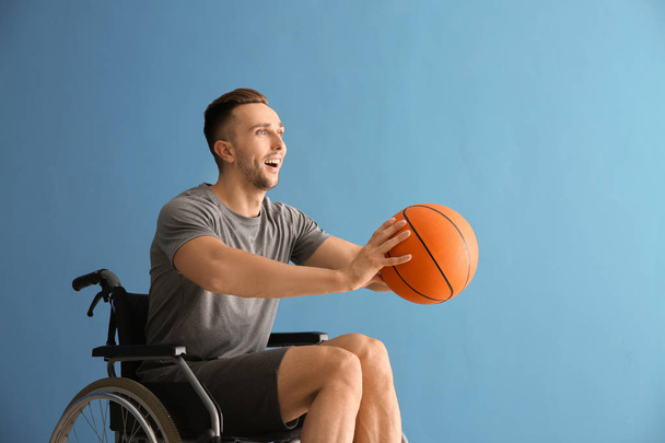 Joven jugador de baloncesto sentado en silla de ruedas contra fondo de color
 - Foto, Imagen