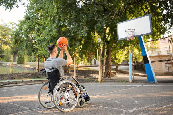 Молодой человек в инвалидной коляске играет в баскетбол на открытом воздухе
 - Фото, изображение