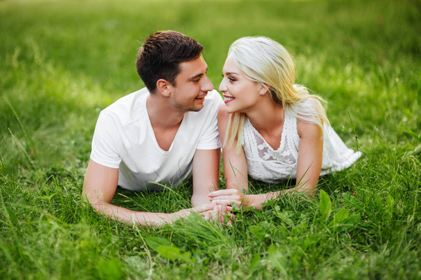 The lovely beautiful couple in love sitting on green grass. Romantic love story in the park. Young girl and boy in love. - Fotoğraf, Görsel