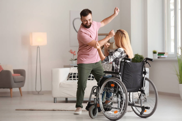Piękna kobieta na wózku inwalidzkim z mężczyzną dancing w domu - Zdjęcie, obraz