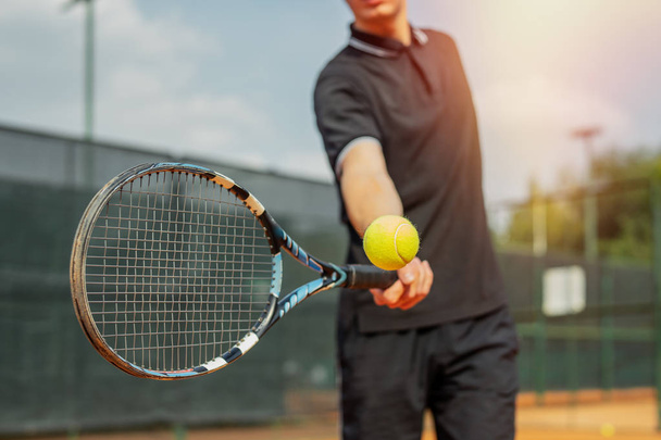 Close up of young attractive man playing tennis at tennis court and beating the ball with a racket. Player is hitting ball with racket while playing match. - Foto, afbeelding