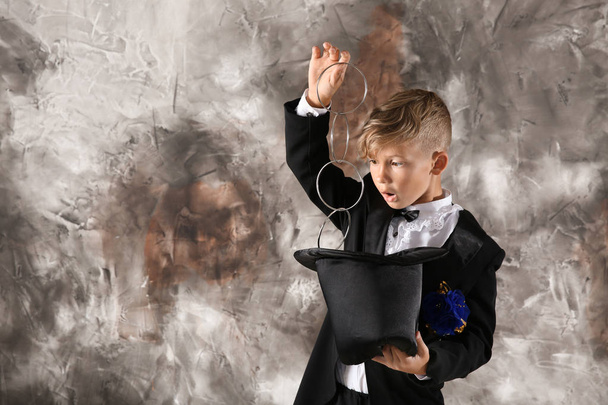 Cute little magician showing trick with hat on grunge background - Photo, Image
