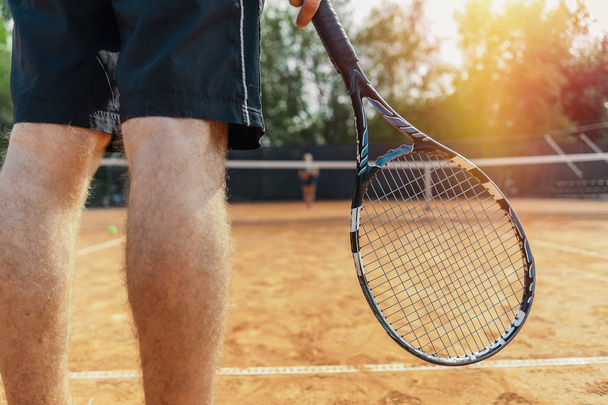 Close up of man holding racket while waiting for ball serving at tennis court. Man is on focus and foreground, tennis net is on background and blurred. - Foto, afbeelding