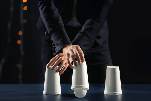 Magician showing tricks with cups on dark background - Photo, Image