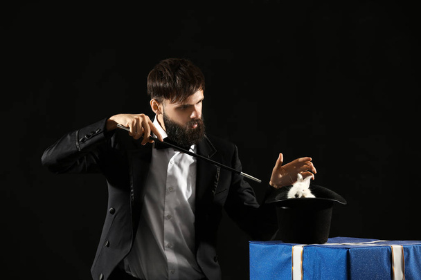 Magician showing tricks with rabbit on dark background - Photo, Image