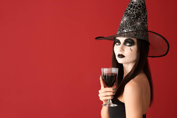 Beautiful woman dressed as witch for Halloween with wine on color background - Foto, immagini