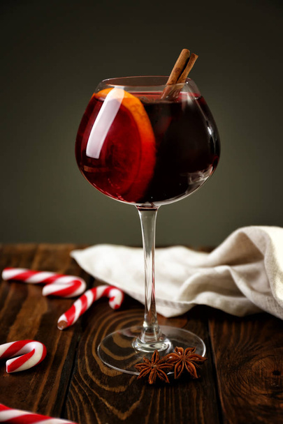 Glass of delicious mulled wine on wooden table against dark background - Valokuva, kuva