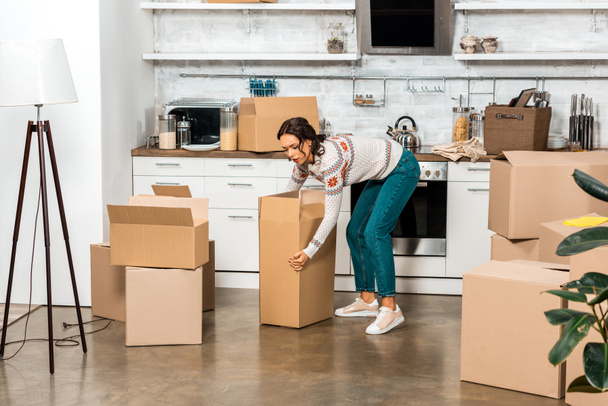 young woman taking cardboard box during relocation in new home  - Foto, immagini