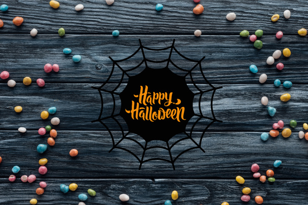 elevated view of arranged colorful delicious candies on wooden background with spider web and "happy halloween" lettering - Photo, Image