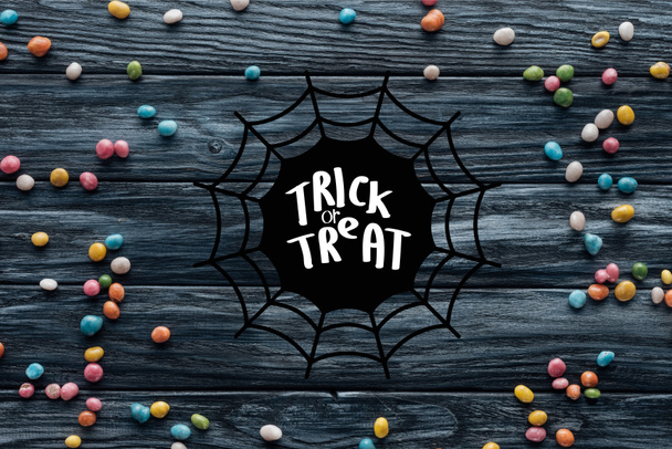 elevated view of arranged colorful delicious candies on wooden background with spider web and "trick or treat" lettering - Foto, immagini