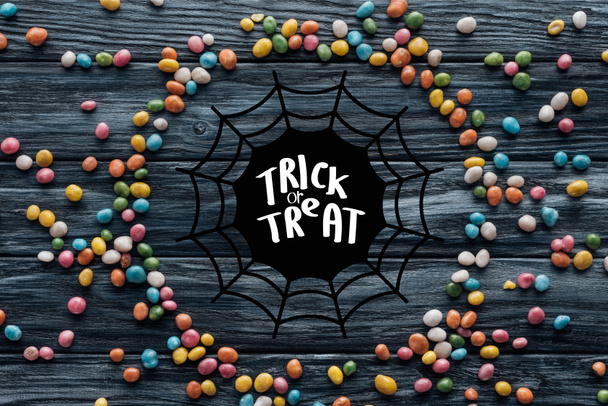 circle made of colorful delicious candies on wooden background with spider web and "trick or treat" lettering - Photo, Image