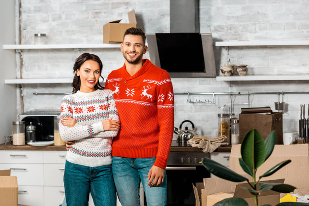 gelukkige jonge paar staande in de keuken met karton vakken in nieuwe woning  - Foto, afbeelding