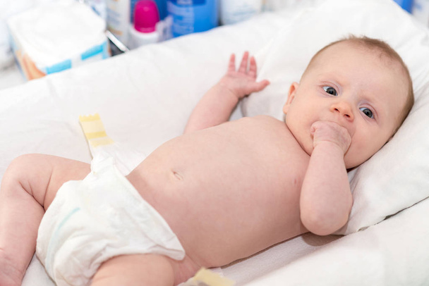 Portrait of cute baby girl in diaper lying on changing table - Fotó, kép