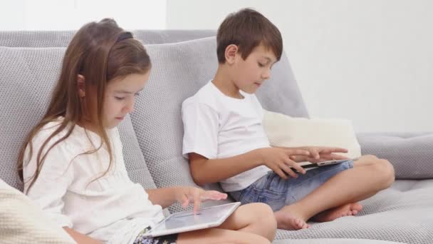 Two kids with gadgets. Sister and brother surfing the net or playing online games on digital tablets at home. Side view - Кадры, видео