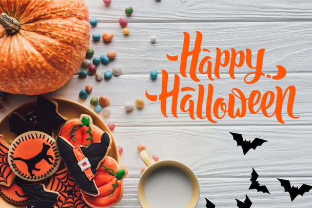 top view of pumpkin, plate with halloween cookies, candies and cup with milk on wooden table  with bats and "happy halloween" lettering - Foto, imagen