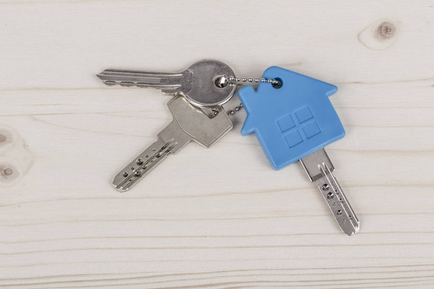 Ключи с голубым ключом в форме дома на деревянном столе
 - Фото, изображение