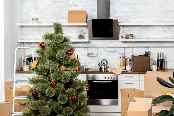 interieur van de keuken met versierde kerstboom en kartonnen dozen tijdens verhuizing nieuwe thuis  - Foto, afbeelding