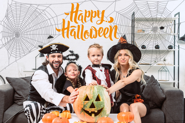 Familienporträt in verschiedenen Halloween-Kostümen am Kaffeetisch mit Kürbissen zu Hause mit "Happy Halloween" -Schriftzug - Foto, Bild