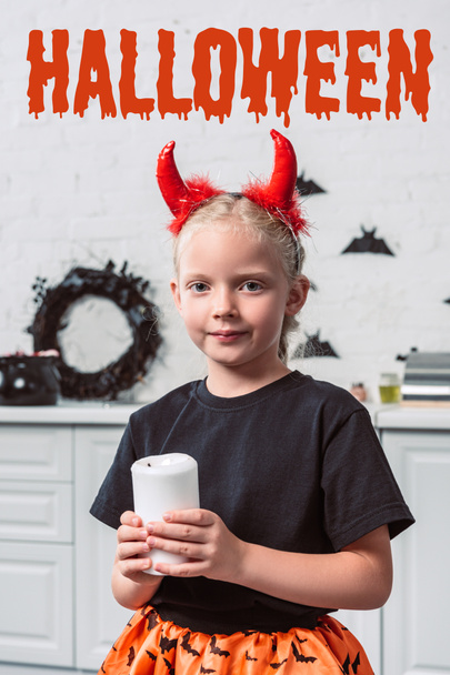 Portret van klein kind met rode duivel hoorns kaars in handen thuis, bedrijf met "halloween" belettering - Foto, afbeelding