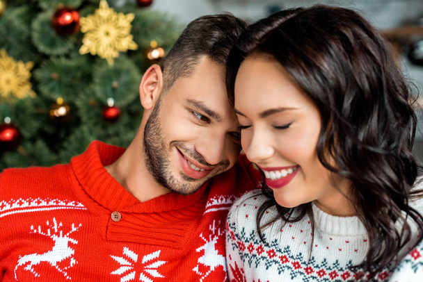 επιλεκτική εστίαση του χαμογελώντας νεαρό ζευγάρι κοντά στολισμένο χριστουγεννιάτικο δέντρο στο σπίτι  - Φωτογραφία, εικόνα