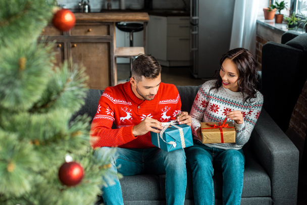selective focus of couple sitting on sofa with gift boxes near christmas tree at home  - Foto, Imagem