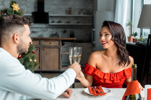 selective focus of happy couple celebrating christmas and clinking by champagne glasses at served table with candles at home - 写真・画像