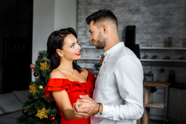 side view of happy young couple looking at each other and dancing on christmas at home  - Valokuva, kuva