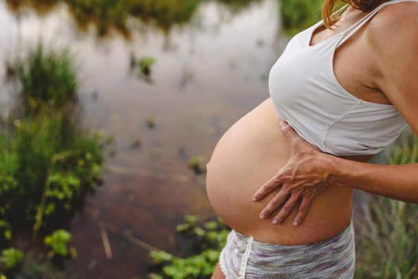 Primer plano del vientre de la mujer embarazada acariciando con sus manos en la naturaleza
. - Foto, Imagen
