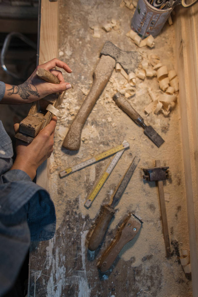 Жіночі руки з татуюваннями роблять дерев'яний продукт у майстерні. Вид зверху
 - Фото, зображення