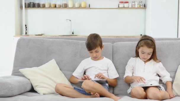 Happy siblings sitting on sofa at home and playing with pc tablet together - Imágenes, Vídeo