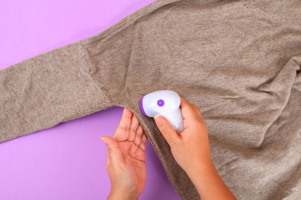 A machine for removing lint in the hand. Sweater with bobble on a purple pastel background - Photo, Image
