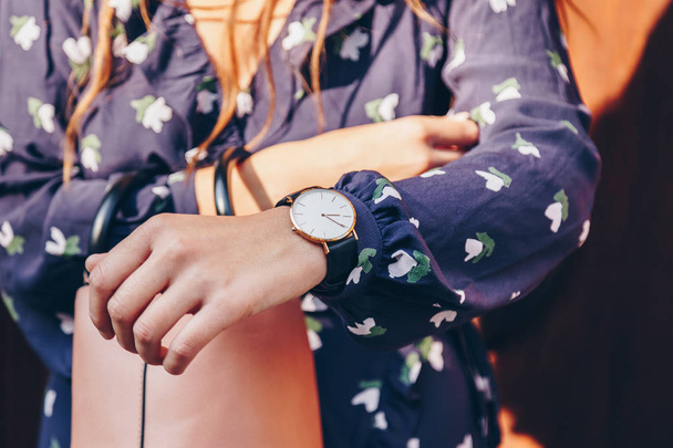 street style fashion details. close up, young fashion blogger wearing a floral dress, and a black and white analog wrist watch. checking the time, holding a beautiful pink purse. - Photo, Image
