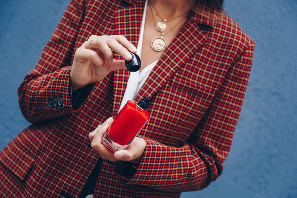 junge Frau mit kariertem Blazer und Münzkette posiert mit einer Flasche teurem Parfüm. schöne und stilvolle europäische Mode-Bloggerin posiert mit Parfüm im Freien. perfektes Herbst-Outfit.  - Foto, Bild