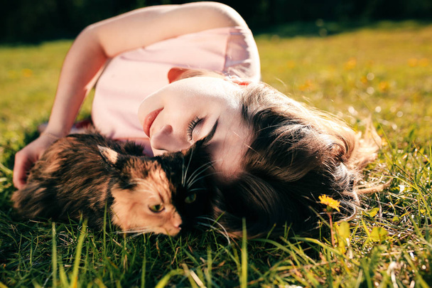 Girl lying on grass with cat. Spring or summer warm weather concept. Bokeh background. Ginger kitten with two face color mask - Photo, Image