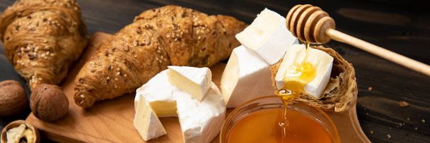 slices of cheese brie or camembert with croissants, honey and nuts on board for cutting, on dark wooden background - Foto, imagen