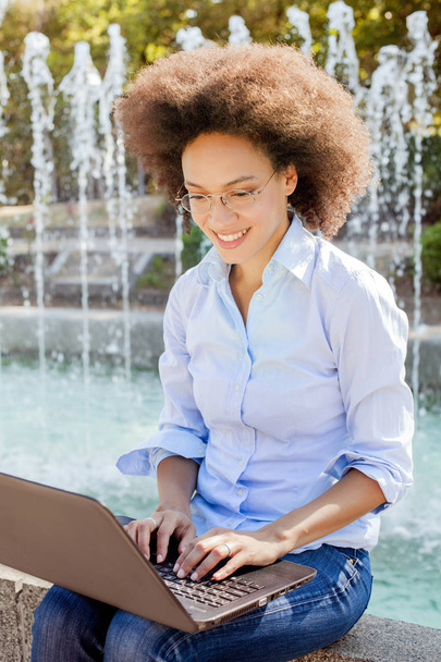 Gülümseyen genç Afro Amerikan öğrenci kadın gözlüklü Laptop ile çalışma. Açık portre, giyim, bilgisayar arıyorum - Fotoğraf, Görsel
