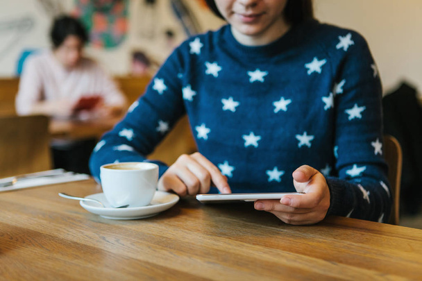 Девушка в кафе пьет кофе и пользуется планшетом
 - Фото, изображение
