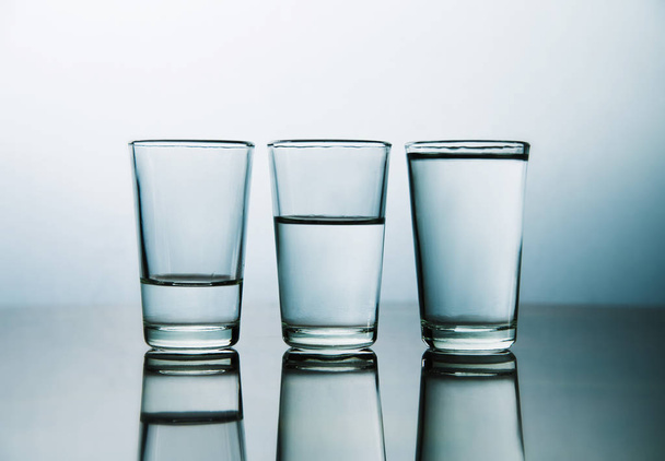 studio shot of three water glasses each one have more water than the other - Foto, Bild