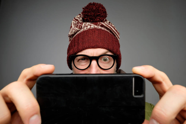 Divertido adulto europeo en sombrero caliente y bufanda hombre usando aplicación de teléfono inteligente. Sesión de estudio
 - Foto, Imagen