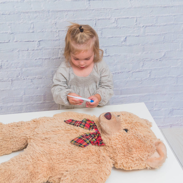 the girl, child measures the temperature of the body of the toy bear, plays doctor - Foto, Imagem