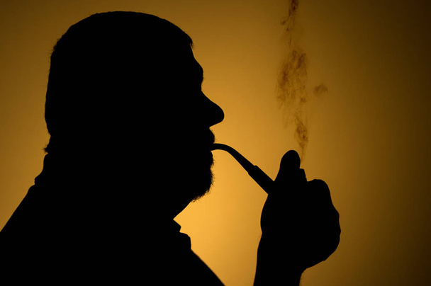 Outline portrait of caucasian bearded man smoking tobacco pipe against sepia background - Photo, Image