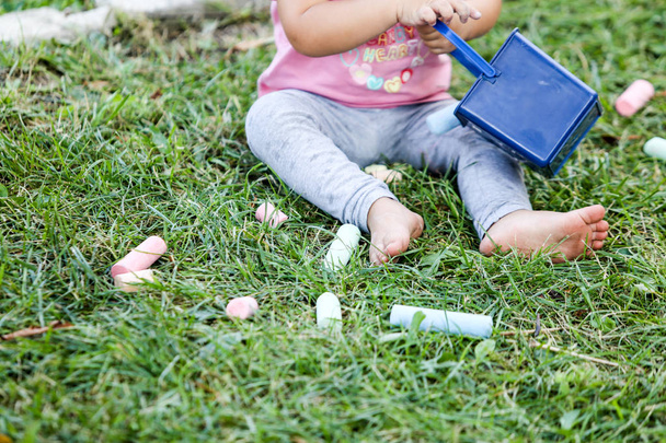 Details of a young girl playing with colored chalk on the grass, in the front yard of a kindergarten in Bucharest, Romania - Фото, изображение