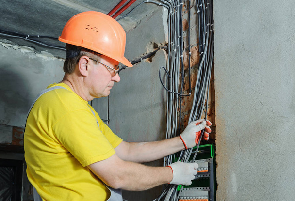 A villanyszerelő telepítése elektromos vezetékek a kapcsolási biztosíték doboz. - Fotó, kép