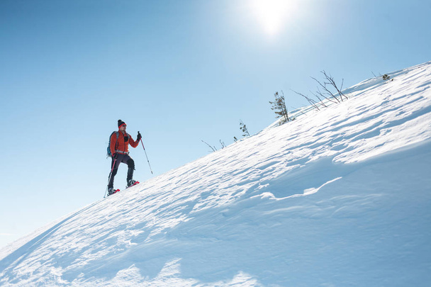男は山の頂上に登っていきます。雪靴のアルピニストは、バックパックを運ぶ。冬の山での旅。自然の中の極端な休暇。極端な条件での観光. - 写真・画像