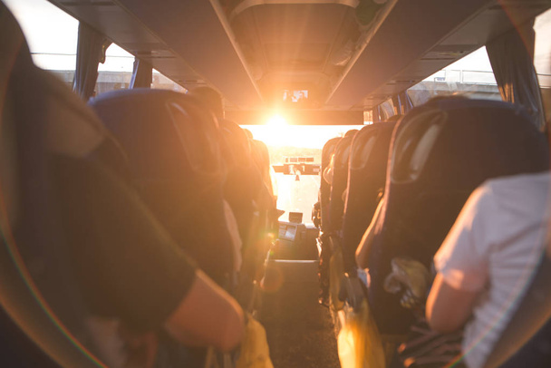 Salon van de kwaliteitsniveaus van de bus met mensen vullen de zon met het licht in de zonsondergang. Mensen reizen op een grote toeristische bus. De bus rijdt langs de ochtenden in de zonsopgang - Foto, afbeelding