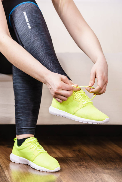 Woman in sportswear sitting on sofa indoor getting ready for exercises. Tying up shoes - Foto, Imagem