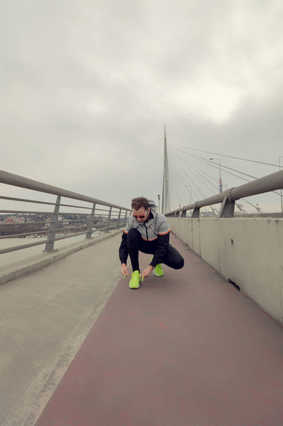 Человек завязывает кроссовки на большом мосту
. - Фото, изображение