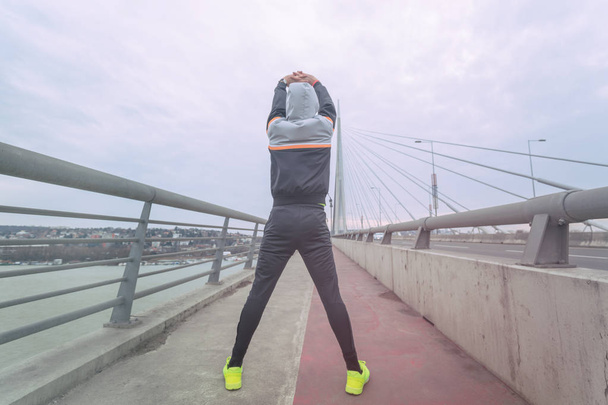 Stedelijke jogger die zich uitstrekt over een grote brug. - Foto, afbeelding